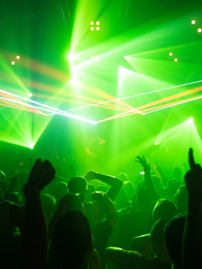 Foule bras levés sur une piste de danse balayée par des lasers verts