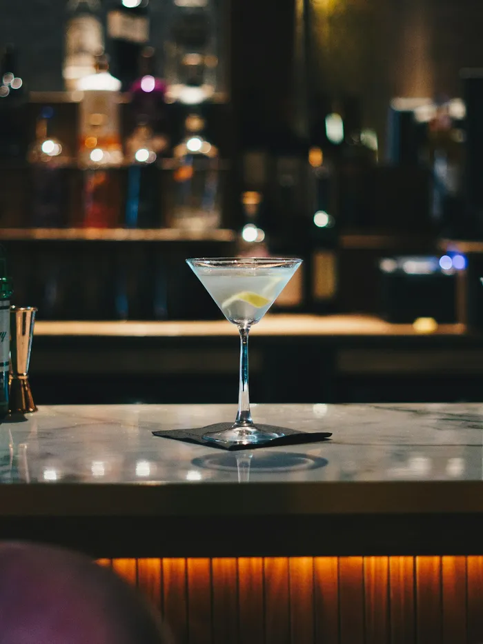Cocktail servi dans un verre à pied sur un comptoir de marbre, bouteilles en arrière-plan